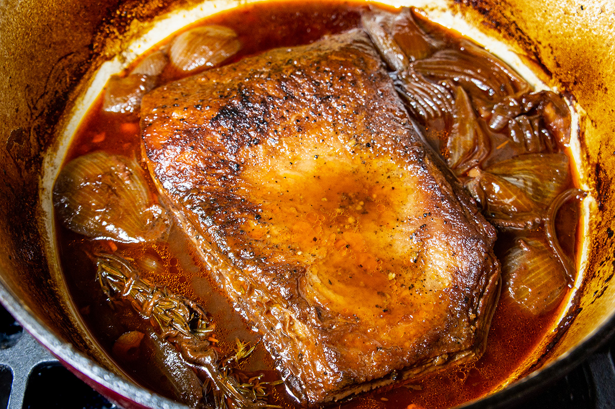 angled shot of brisket slow cooking in dutch oven