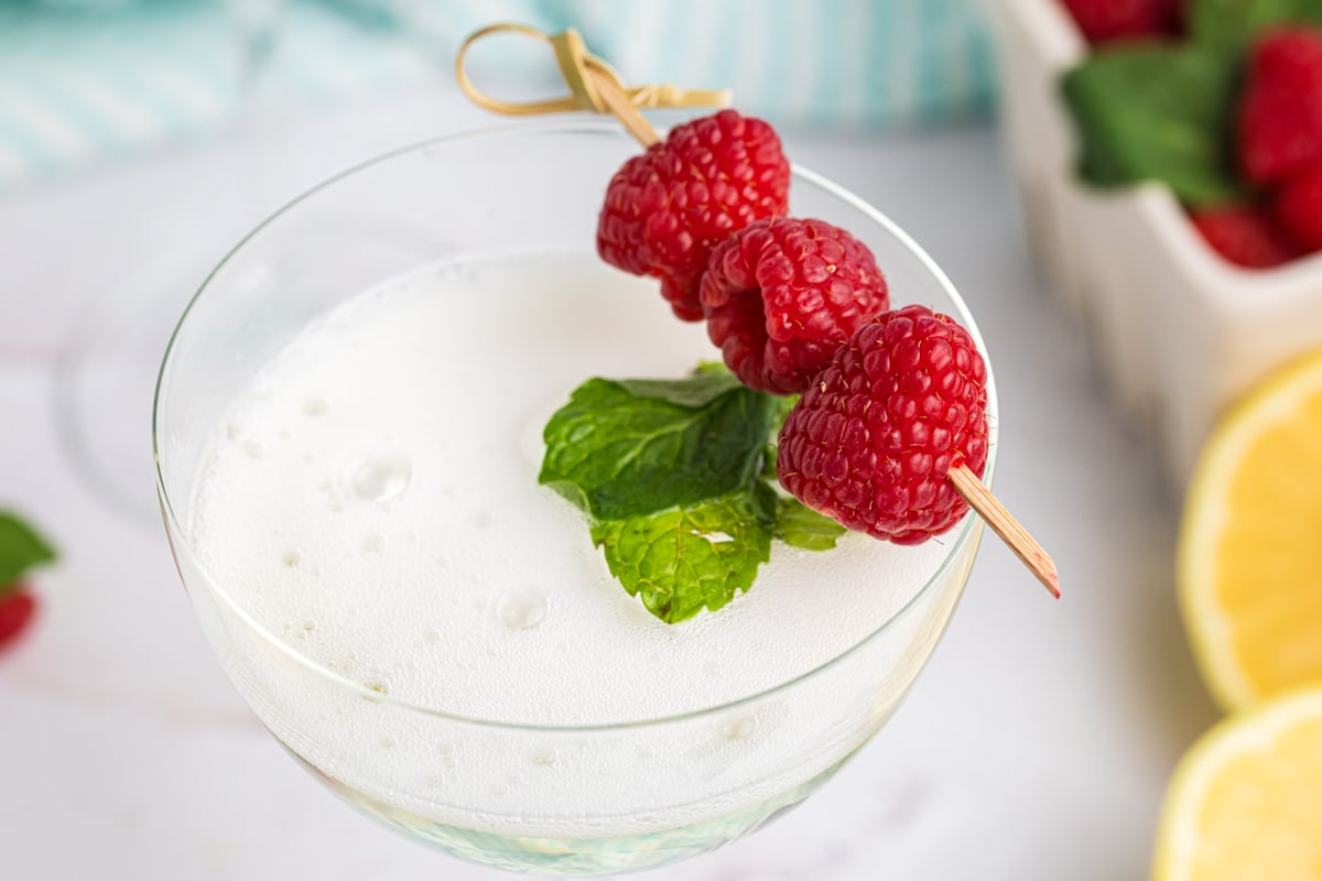 close up angled shot of raspberries and mint in elderflower spritzer