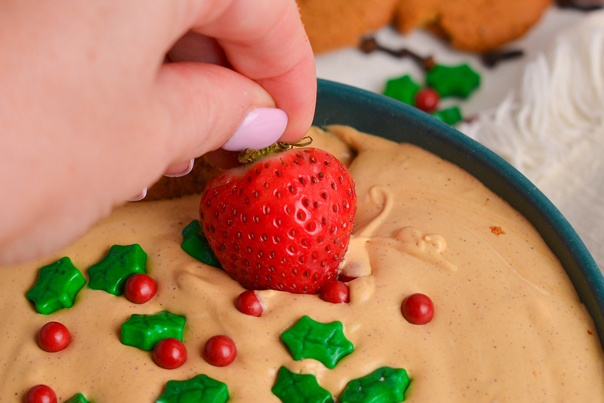 hand dipping strawberry into dessert dip