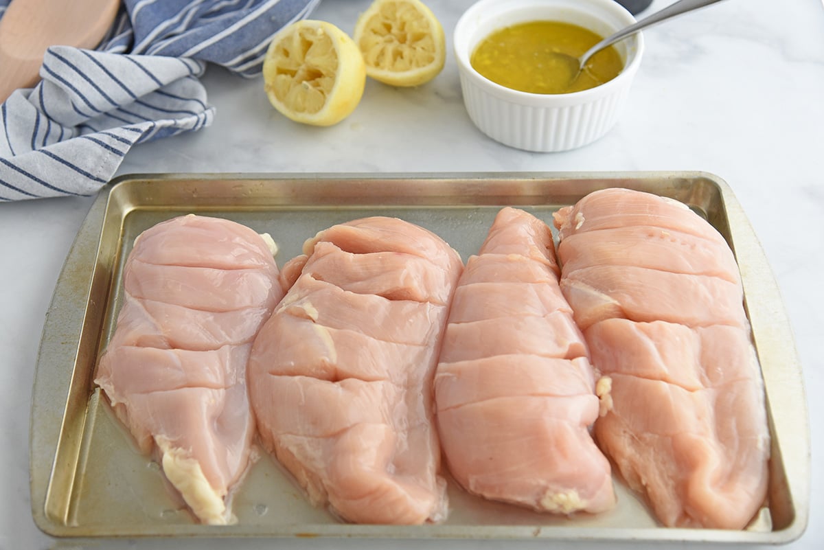 raw scored chicken breasts on baking sheet