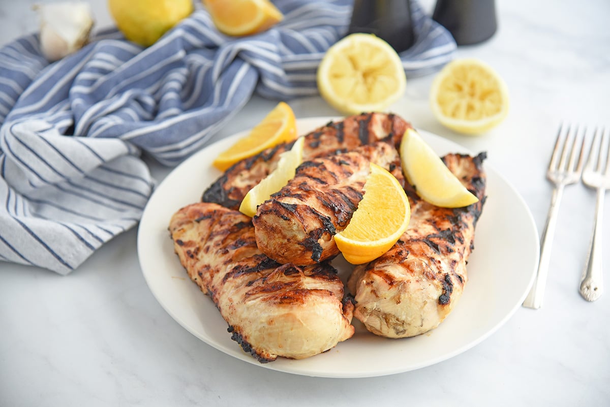 angled shot of grilled citrus chicken on a plate with lemon wedges