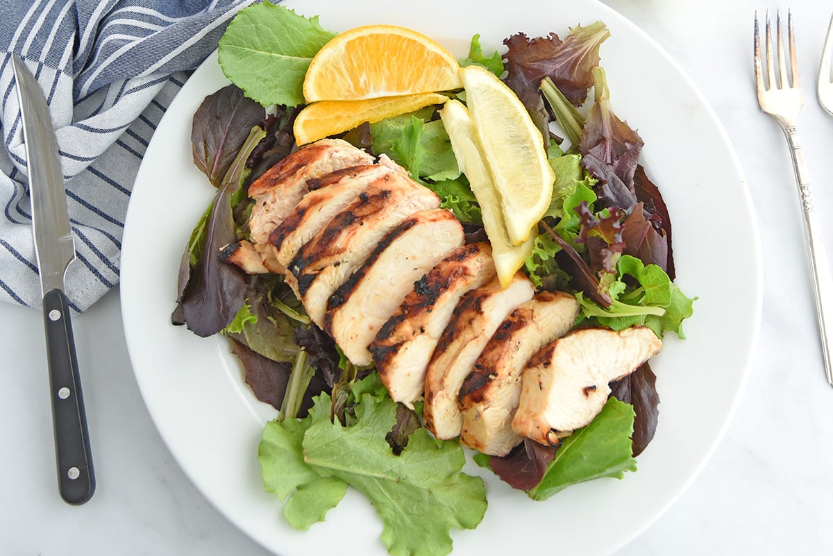 overhead shot of sliced grilled chicken over salad