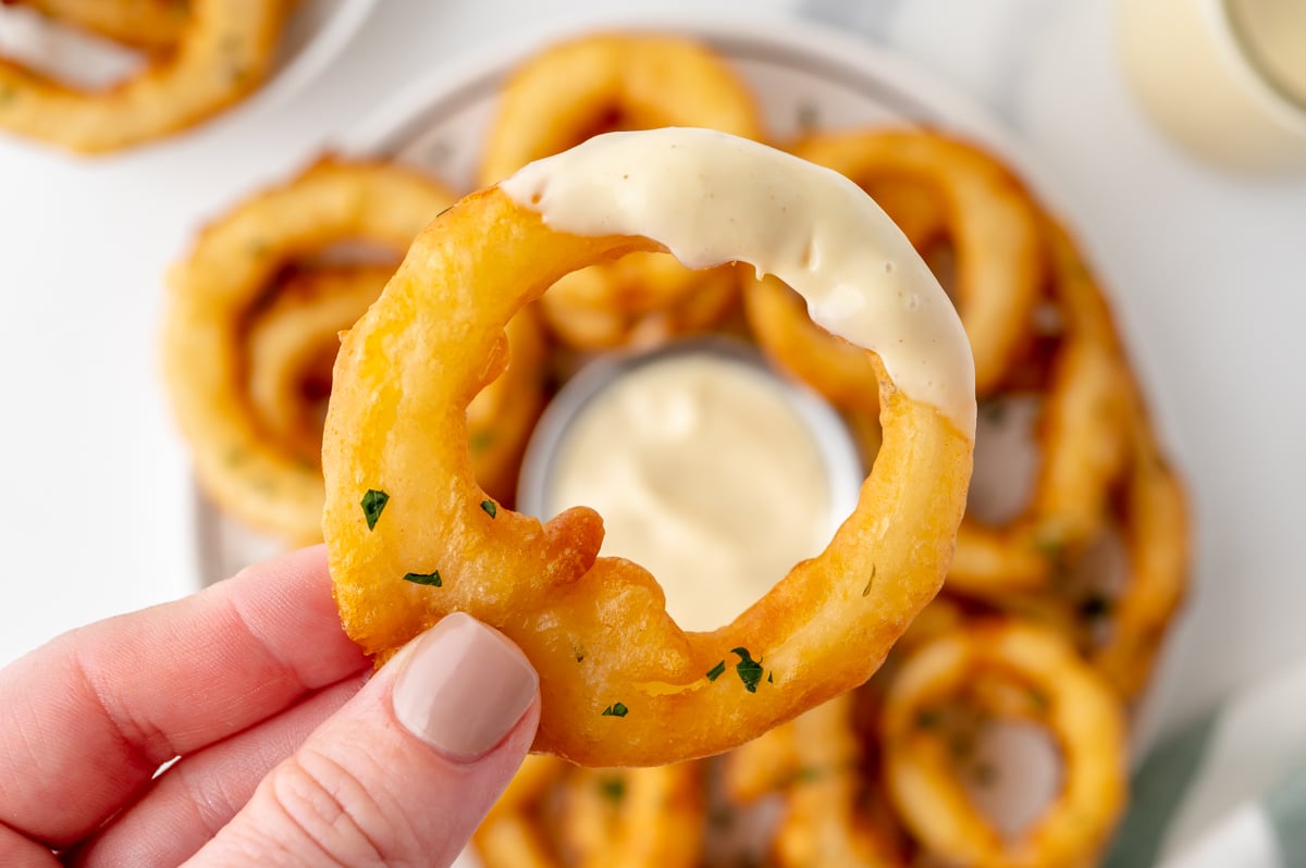 overhead shot of hand holding onion ring dipped in mustard aioli