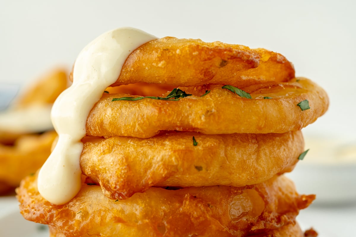 close up straight on shot of stack of beer battered onion rings with sauce dripping down