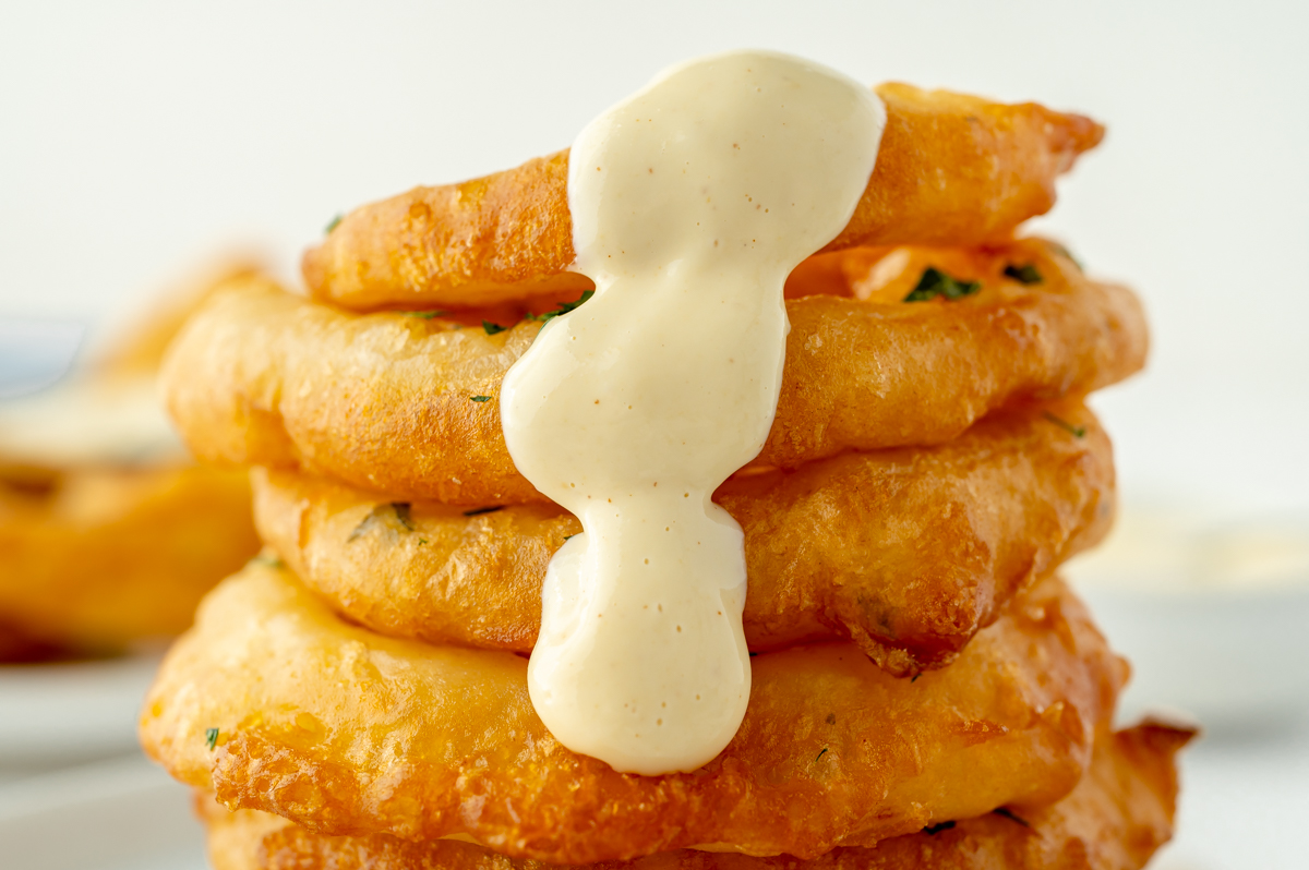 straight on shot of stack of beer battered onion rings with sauce dripping down