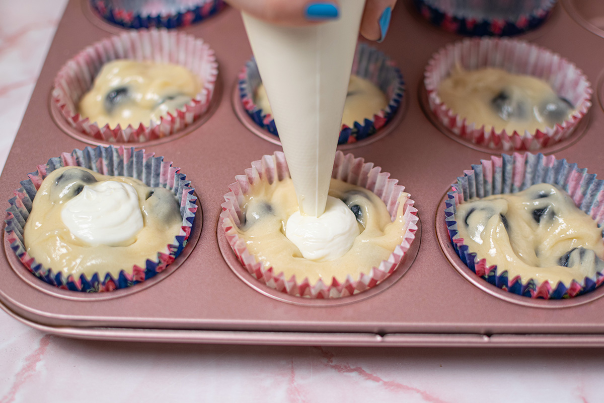 piping bag adding cream cheese filling to muffin batter in pan