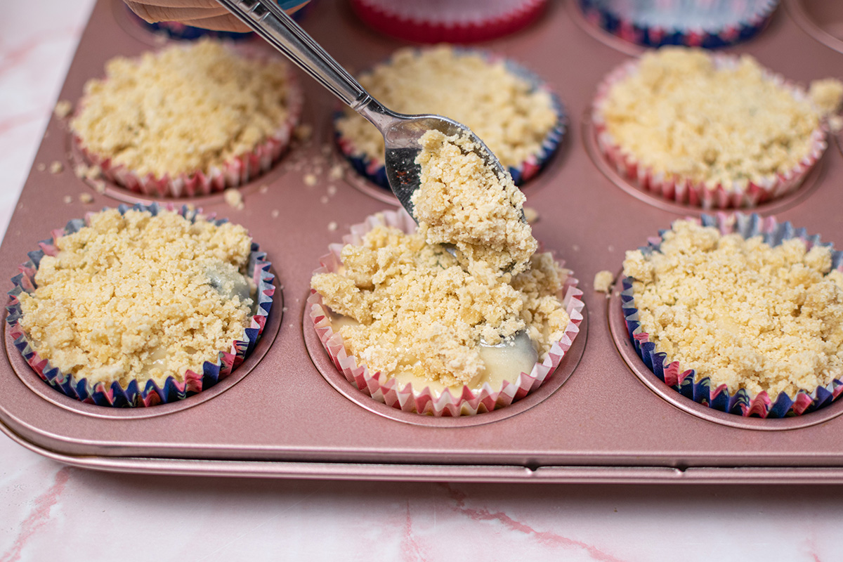 angled shot of spoon adding streusel topping to muffins in pan