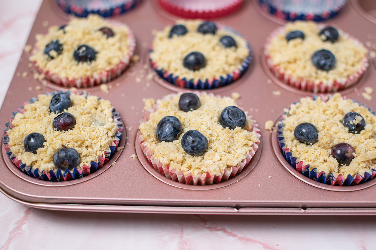 angled shot of blueberries on top of muffins in pan