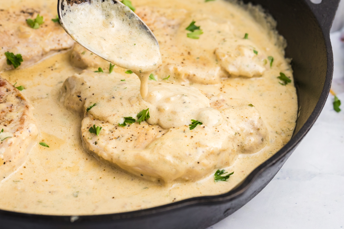 close up angled shot of spoon adding creamy sauce to pork chops