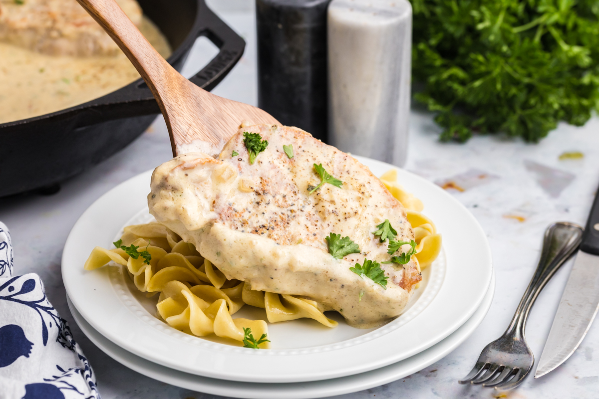 spatula adding boursin pork chop to plate of noodles