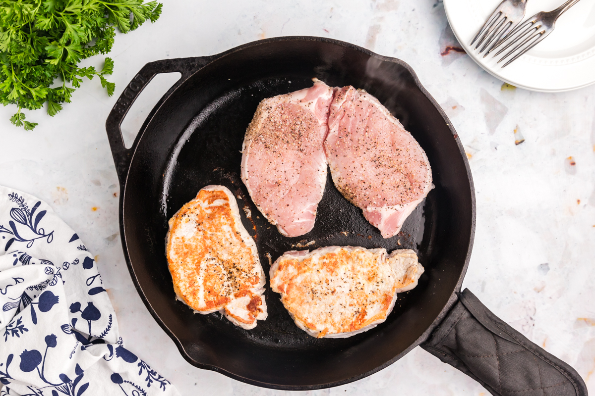 pork chops cooking in cast iron skillet