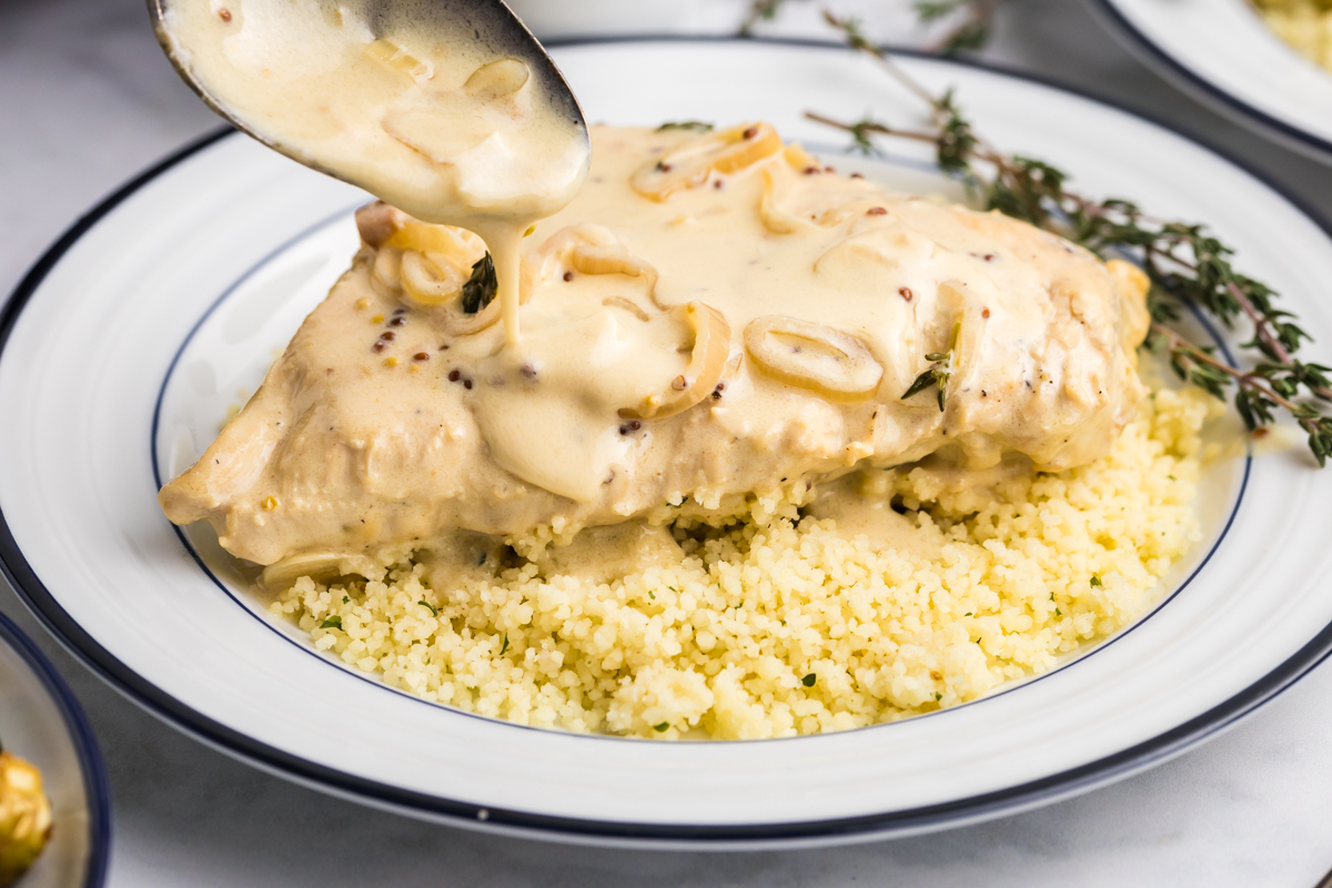 spoon adding creamy sauce to chicken