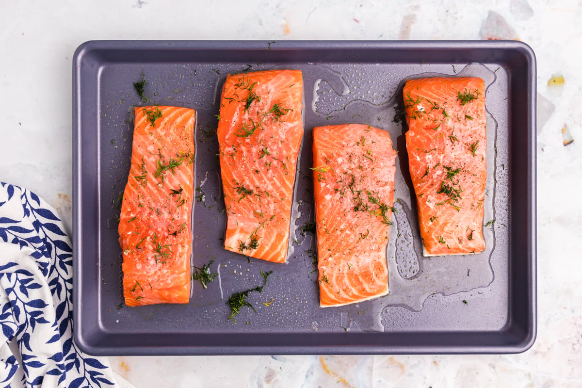 overhead shot of four salmon fillets on baking sheet topped with dill