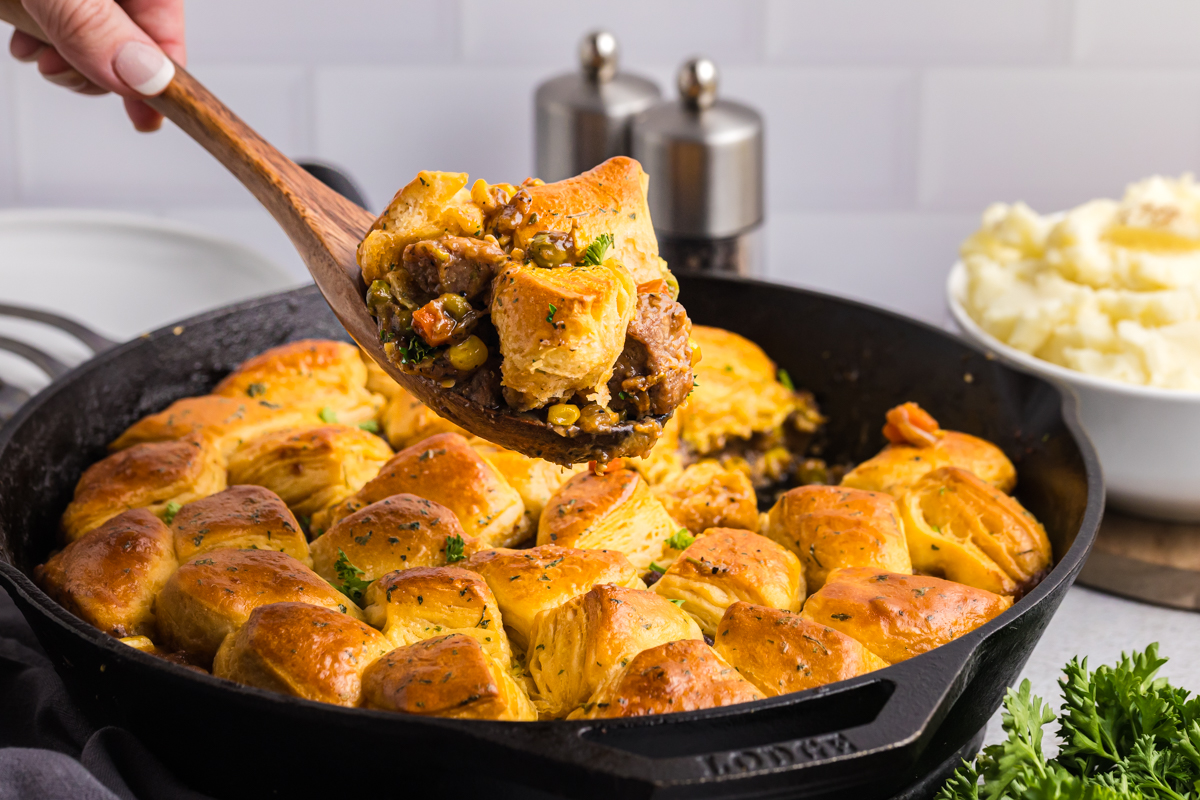 angled shot of wooden spoon scooping out beef pot pie from skillet