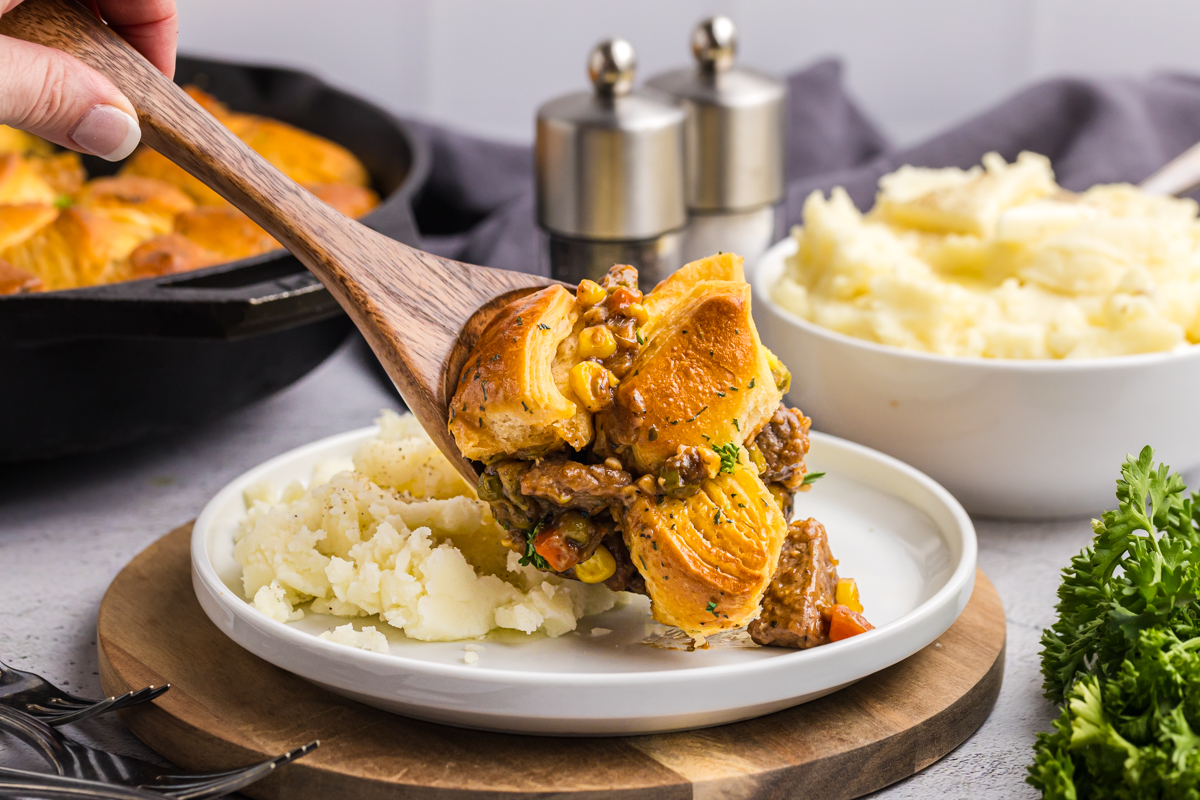 wooden spoon adding beef pot pie to plate