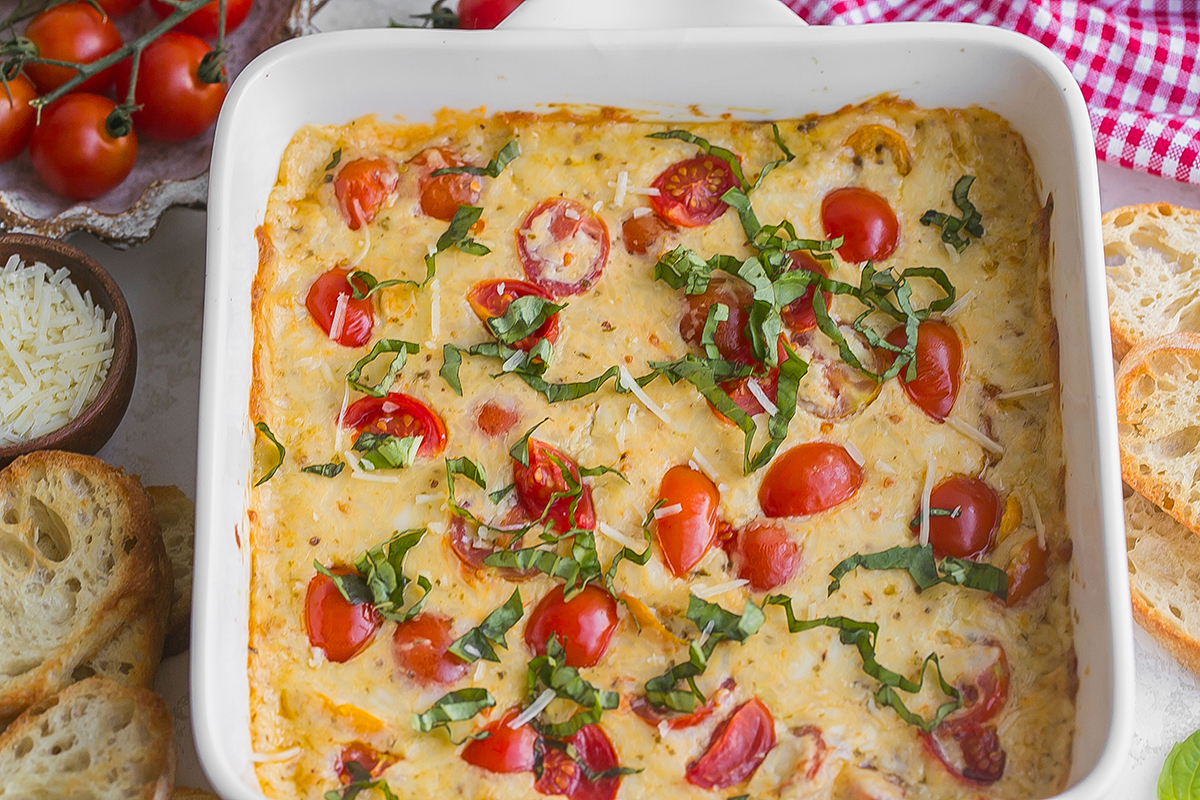 angled shot of baking dish of hot caprese dip topped with fresh basil