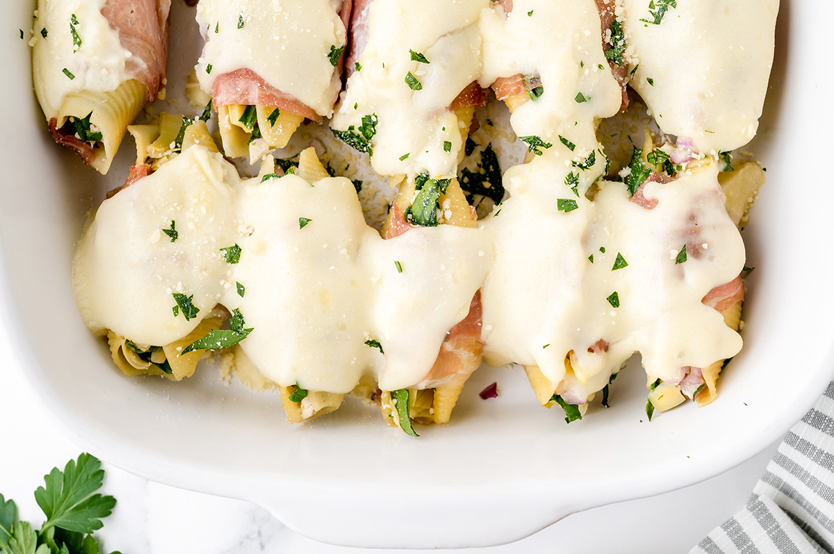 overhead shot of chicken stuffed shells topped with brie sauce in baking dish