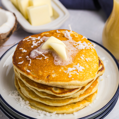 angled shot of stack of pancakes topped with coconut and butter