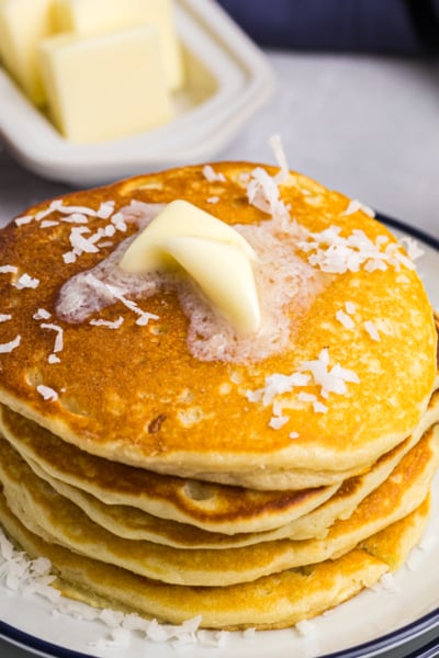 angled shot of stack of pancakes topped with coconut and butter