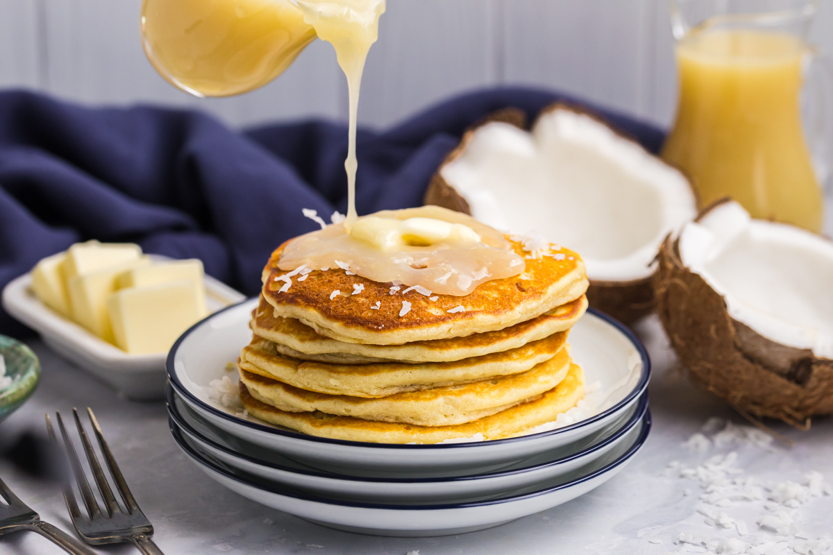 straight on shot of syrup pouring over stack of pancakes