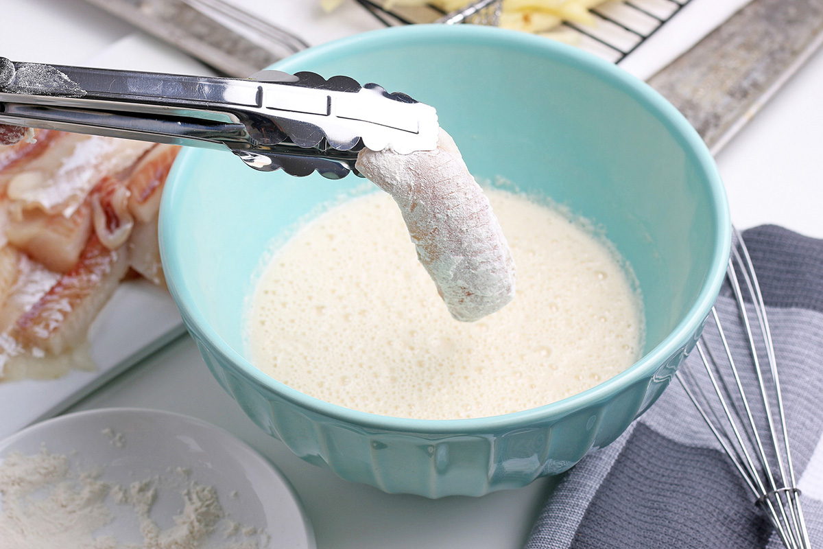 tongs holding fish over bowl of batter