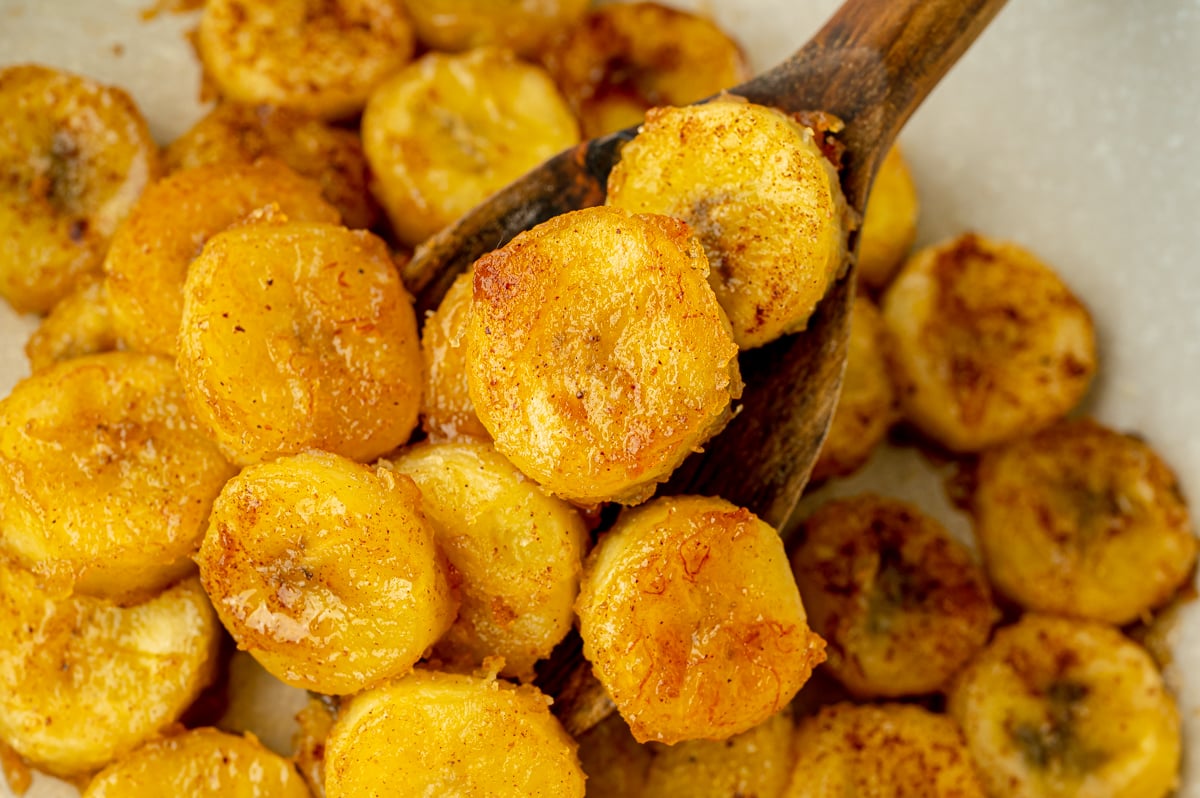 angled shot of wooden spoon in pan of fried bananas