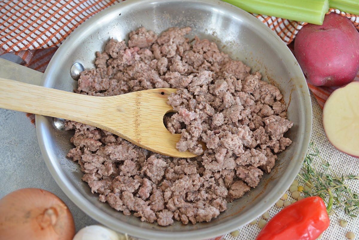 ground lamb browning in skillet with wooden spoon