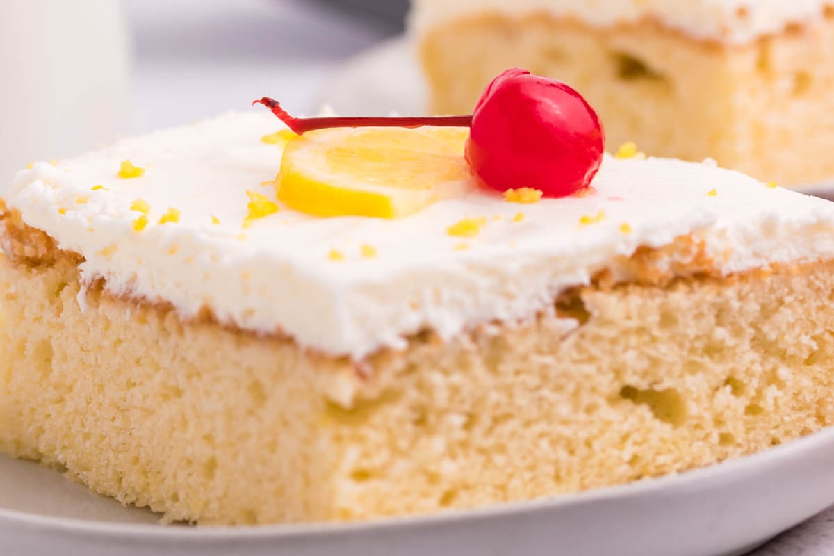 close up shot of slice of lemon sheet cake topped with cherry on plate