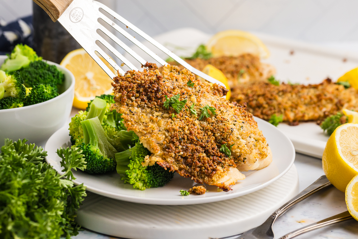 spatula adding breaded tilapia to plate with broccoli