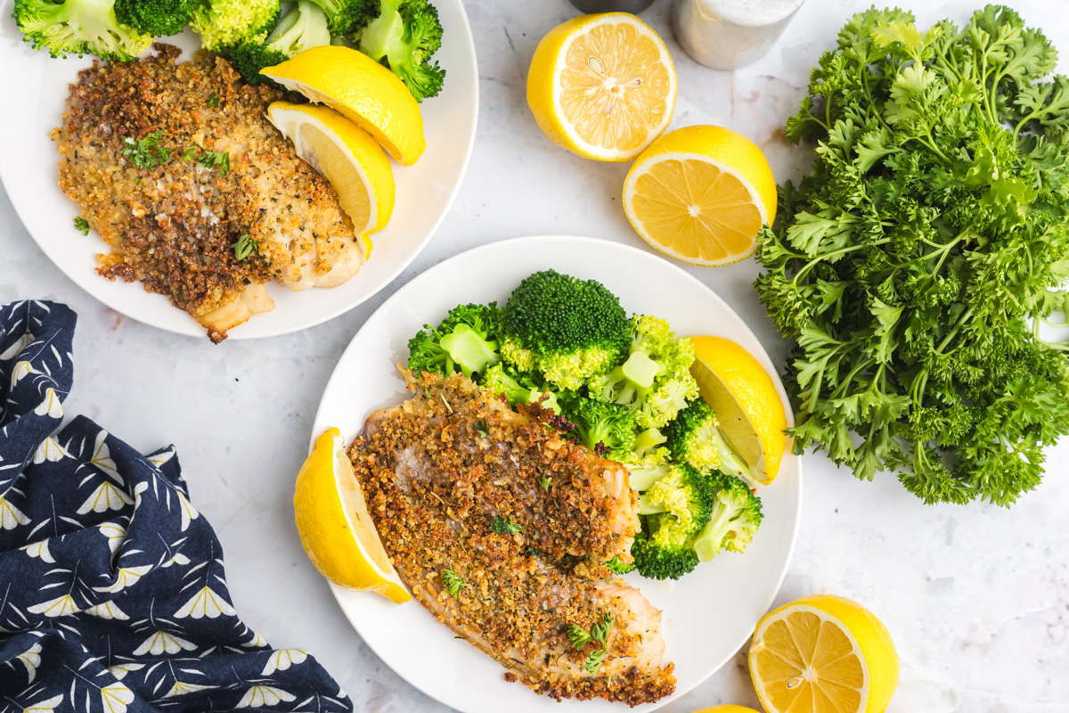 overhead shot of two plates of parmesan crusted tilapia with broccoli