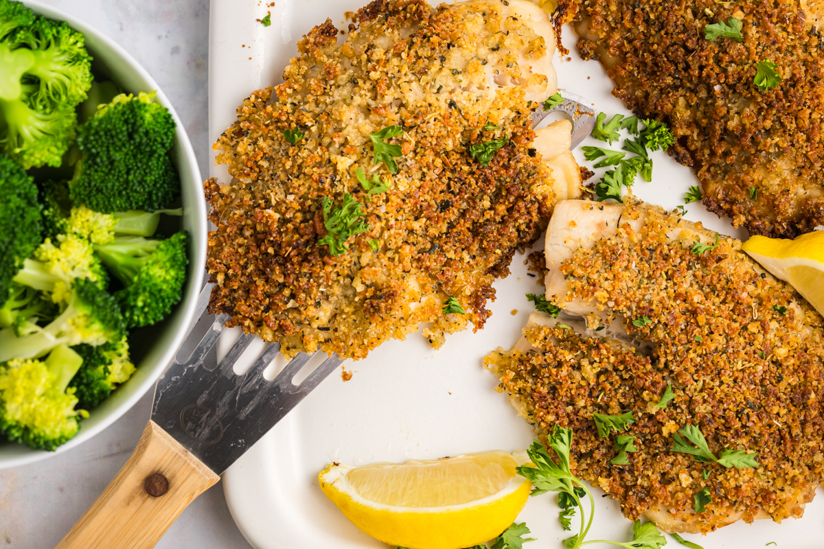 overhead shot of breaded tilapia on tray with lemon wedges