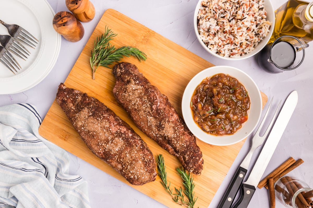 overhead shot of two pork tenderloins on cutting board with bowl of date chutney