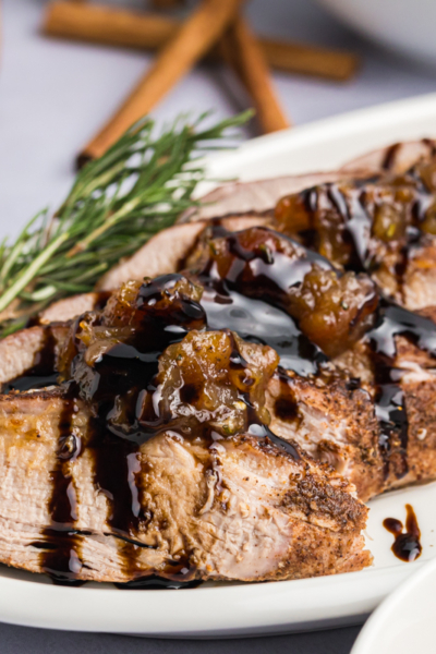 close up angled shot of sliced pork tenderloin on platter with rosemary