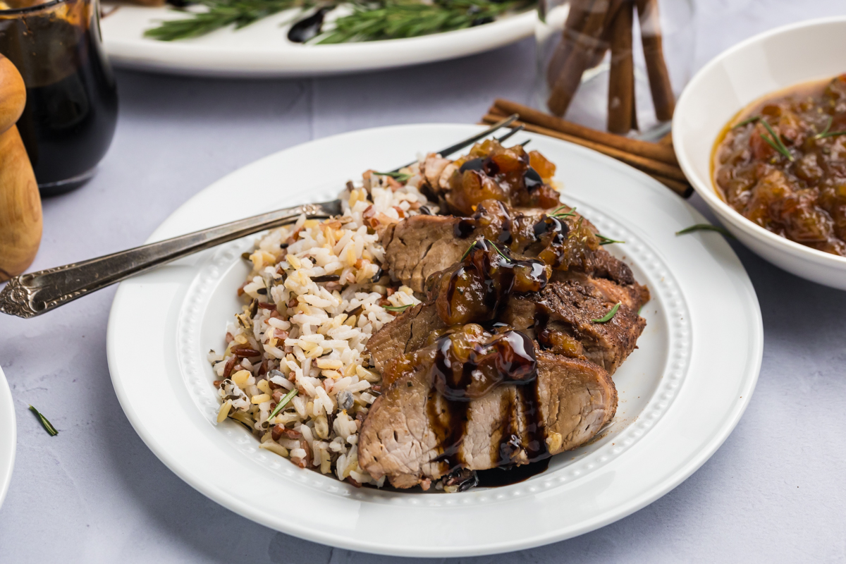 angled shot of sliced pork tenderloin with date chutney on plate with rice