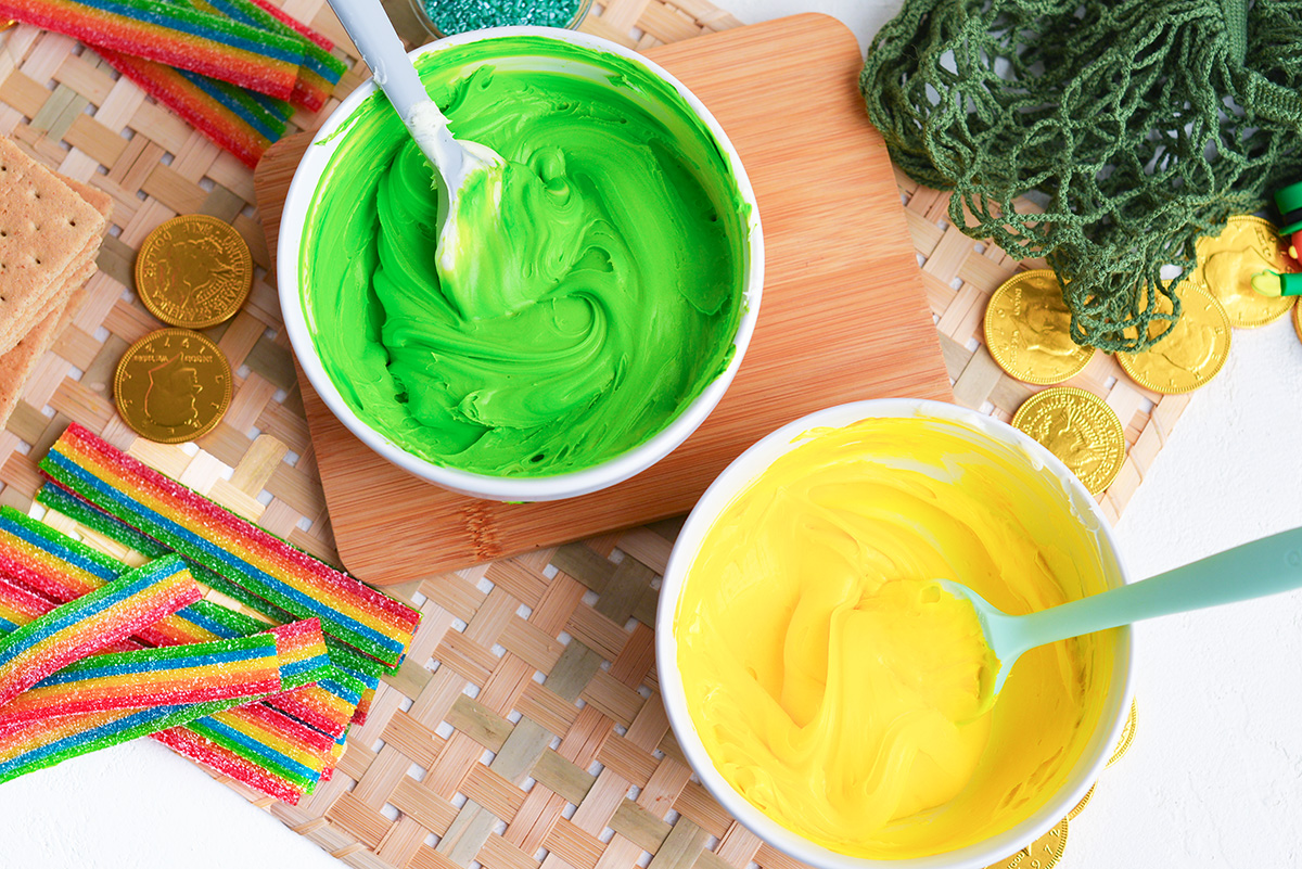 overhead shot of one bowl of green frosting and one bowl of yellow frosting