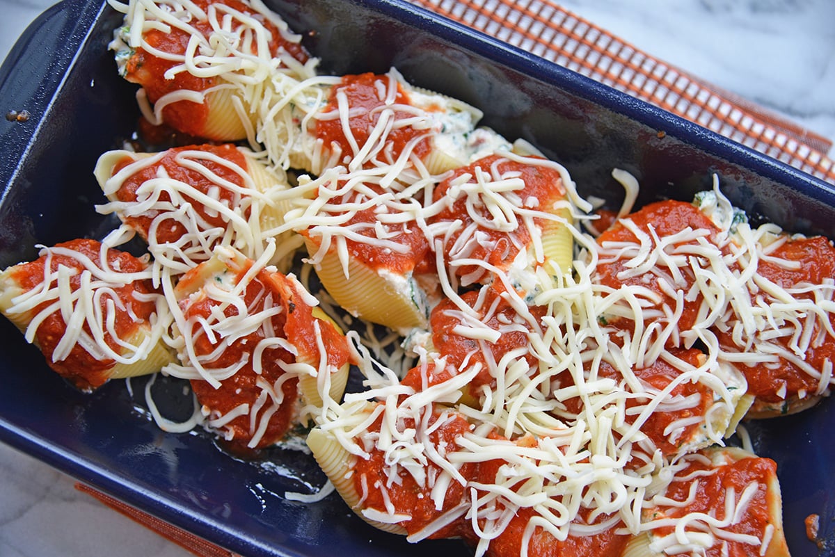 overhead shot of spinach stuffed shells topped with sauce and cheese in blue baking dish