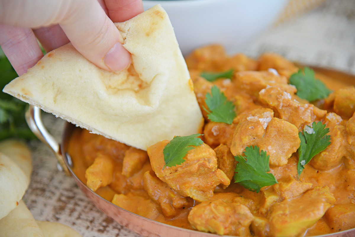 close up shot of pita bread dipping into butter chicken