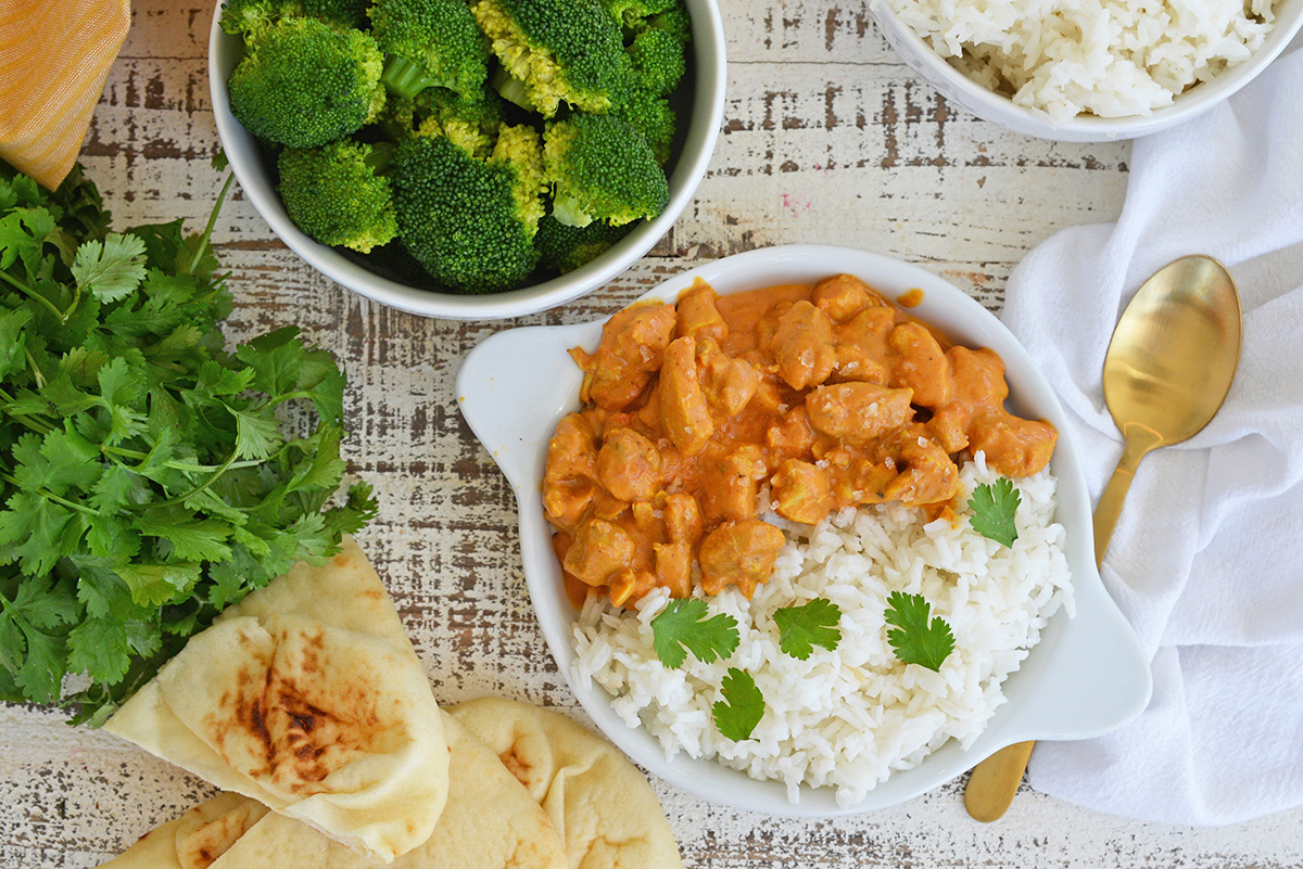 overhead shot of indian butter chicken with rice with bowl of broccoli