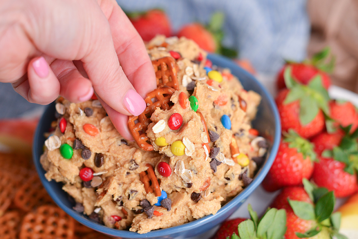 hand dipping pretzel into bowl of dessert dip