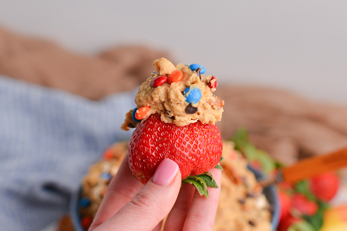 hand holding strawberry with monster cookie dip on it