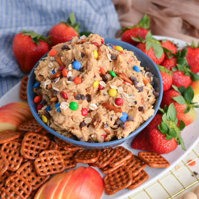 angled shot of bowl of monster cookie dip with pretzels, strawberries and apples