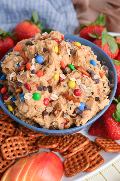 angled shot of bowl of monster cookie dip with pretzels, strawberries and apples