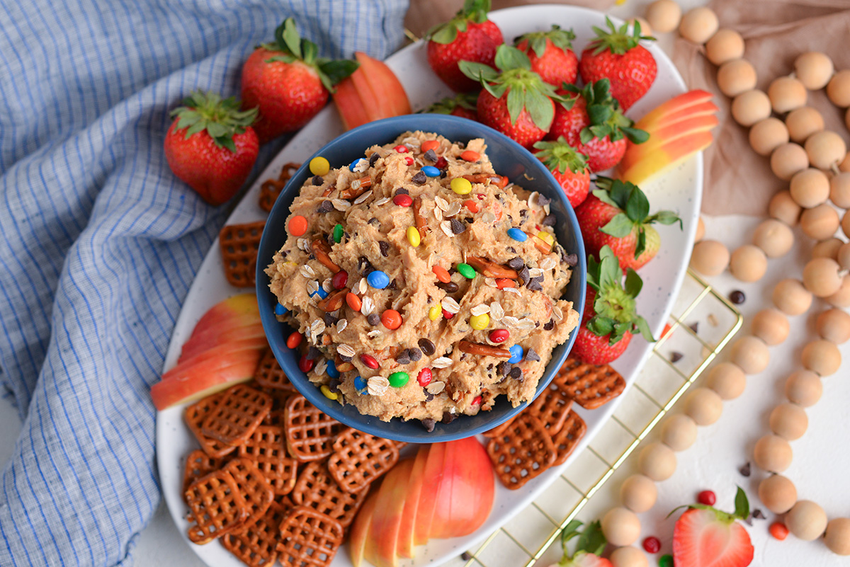 overhead shot of bowl of monster cookie dip with pretzels, strawberries and apples