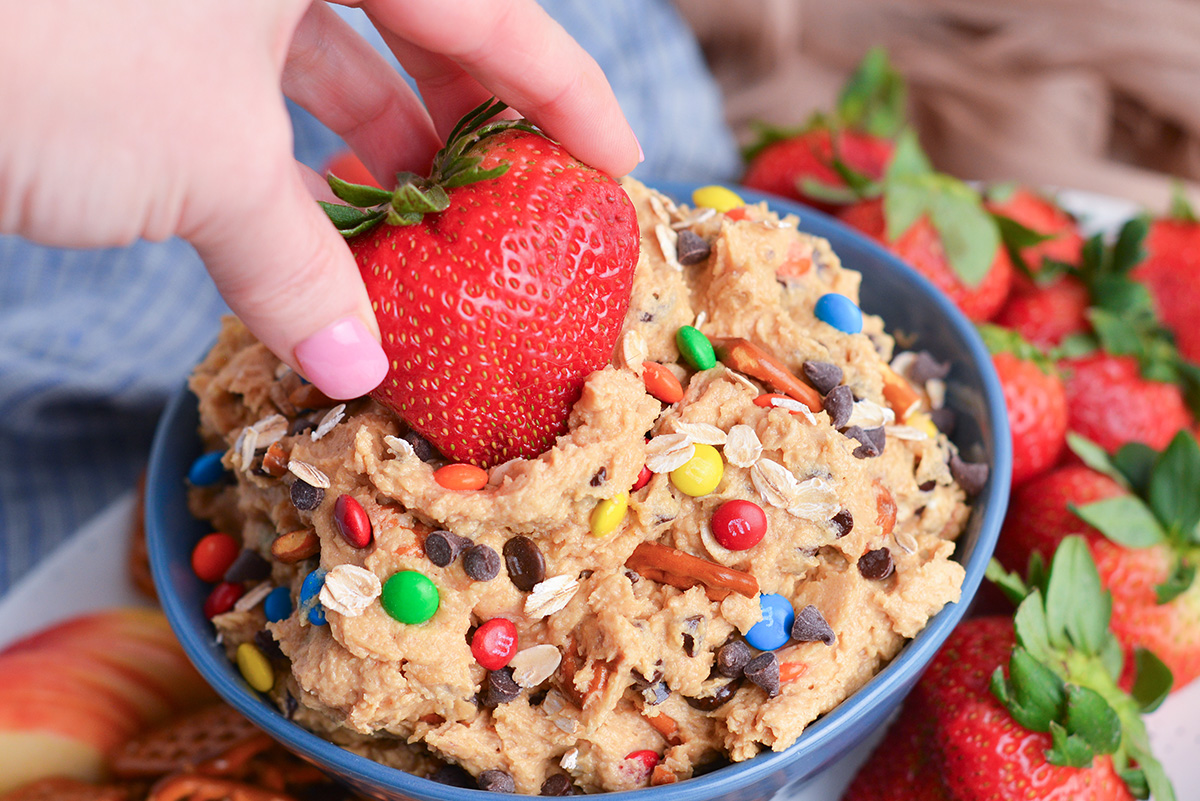 hand dipping strawberry into bowl of monster cookie dip