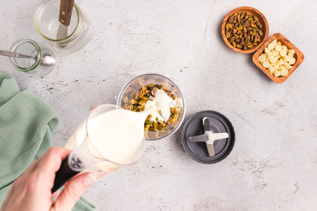 overhead shot of cream pouring into blender with pistachios