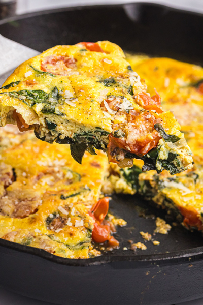 angled shot of slice of tomato spinach frittata on spatula